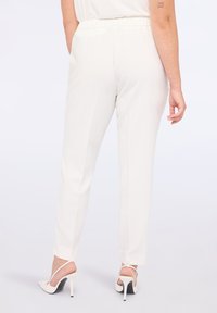 Bílé kalhoty na míru s elastickým pasem, slim fit a bočními rozparky na lemu, doplněné otevřenými podpatky.