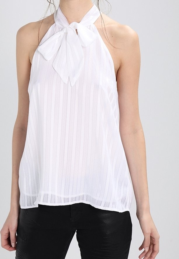 Femme portant un haut halter blanc sans manches à rayures verticales avec un nœud noué au niveau de l'encolure, associé à un pantalon noir.
