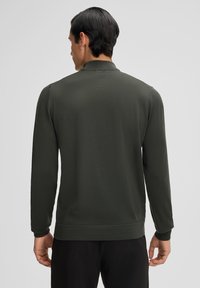 Dunkelgrüner Pullover mit langen Ärmeln, einem Kragen und einer glatten Textur. Verfügt über gerippte Bündchen und Saum, von hinten mit minimalen Details zu sehen.