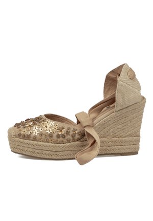 Sandalia espadrille de cuña beige con suela trenzada de cuerda, flores decorativas con lentejuelas en la puntera y cierre de lazo que envuelve el tobillo.