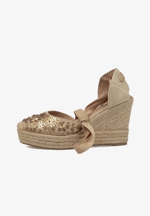 Sandalia espadrille de cuña beige con suela trenzada de cuerda, flores decorativas con lentejuelas en la puntera y cierre de lazo que envuelve el tobillo.