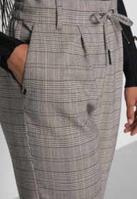 Grå rutiga byxor med en texturerad tyg, veckad front, justerbart midjeband och sidofickor, med kontrasterande svarta detaljer.