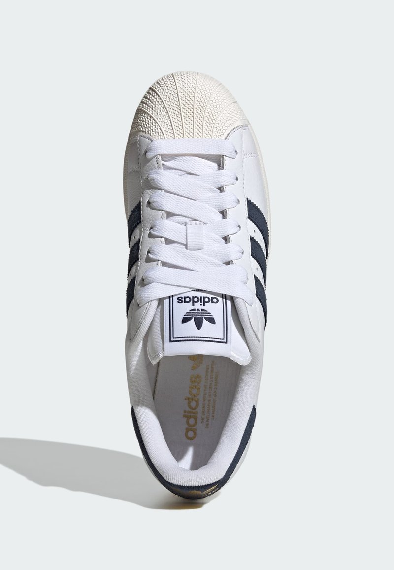 White Adidas sneaker with black stripes, shell toe design, white laces, and logo on tongue and insole, photographed from above on light background.