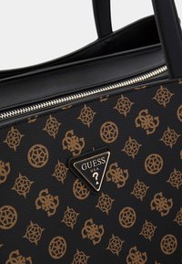 Zwarte synthetische draagtas met gouden logo en ingewikkeld patroon met in elkaar grijpende emblemen en geometrische vormen. Ritssluiting.