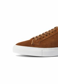 Smeđe suede tenisice s okruglim vrhom, bijelim gumenim potplatom i ravnim vezicama. Imaju suptilne šavove i minimalistički dizajn.