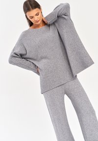 Szary dziany sweter z szerokimi rękawami, w połączeniu z dopasowanymi szarymi spodniami typu tapered. Miękka faktura i luźny krój.