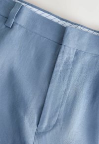 Pantalones cortos de lino azul claro con una textura suave, que cuentan con un solo plisado, cinturilla con trabillas para cinturón y un forro interior a rayas.