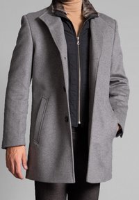 Abrigo de lana gris con solapa muesca, de un solo botón, grandes bolsillos frontales y un suave cuello forrado de piel sobre una chaqueta negra con cremallera.