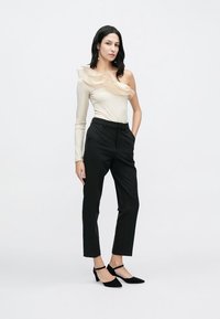 Smėlio spalvos vieno peties palaidinė su raukiniais, derinama su juodomis pritaikytomis kelnėmis ir juodais aukštakulniais; lygios tekstūros ir prigludęs dizainas.