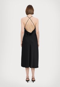 Black satin dress with a draped back, thin crossover straps, and a mid-calf length. Smooth texture and simple design.