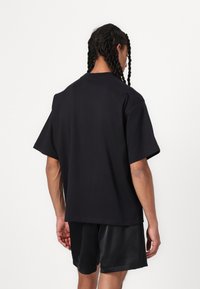 Black oversized t-shirt made of cotton, featuring short sleeves, a crew neck, and a straight hem, worn with satin black shorts.
