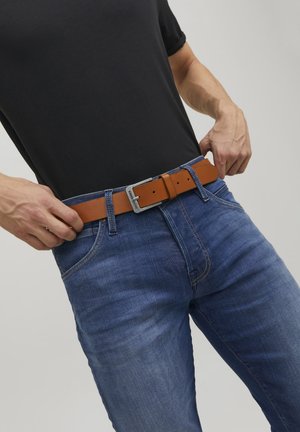 Cinturón de cuero marrón con hebilla de metal, llevado sobre unos pantalones vaqueros azules. La camiseta es negra, de diseño ajustado y con mangas cortas.