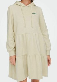 Vestido con capucha, de longitud hasta la rodilla, en tejido beis claro. Presenta volantes recogidos, mangas largas y el texto bordado "low key" en verde en el pecho.