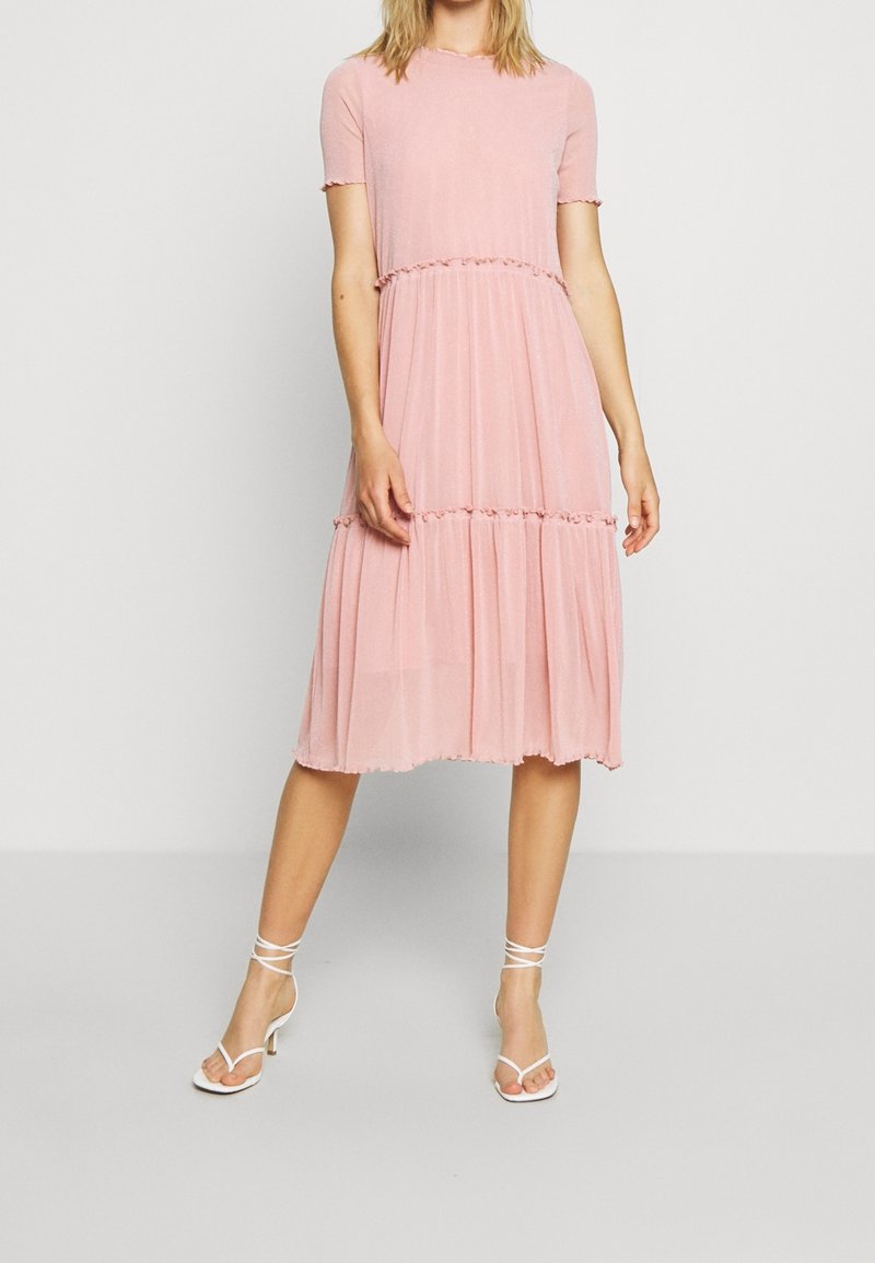 Różowa sukienka na kilka warstw z okrągłym dekoltem i krótkimi rękawami. Materiał ma subtelną teksturę i zdobiony jest falbankami przy szwach.