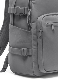 Rucsac gri fabricat dintr-un material durabil; dispune de bretele ajustabile, mai multe buzunare cu fermoar și o cataramă rezistentă. Panou lateral texturat.