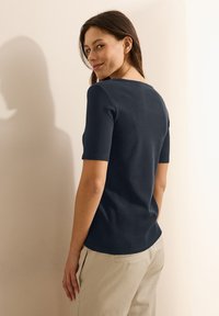 Granatowa bawełniana koszulka z krótkimi rękawami i okrągłym dekoltem. Gładka tekstura, dopasowany krój oraz subtelny detal na plecach.