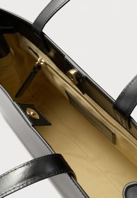 Crna kožna torba s glatkim završetkom; detalji od zlatnog metala; unutrašnjost s bež postavom, džepom na patentni zatvarač i kopčom na magnet.