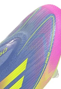 Football boot with a blue and pink gradient design, featuring yellow accents, textured surface, and a cleated sole for traction.