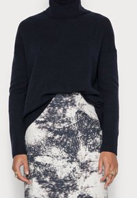 Donkerblauwe turtleneck trui van zachte brei met lange mouwen, gecombineerd met een textuurrijk rok met een monochroom abstract patroon.