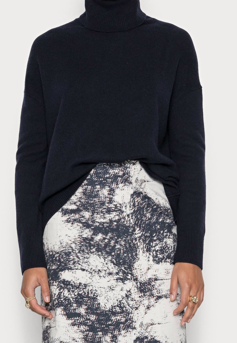 Donkerblauwe turtleneck trui van zachte brei met lange mouwen, gecombineerd met een textuurrijk rok met een monochroom abstract patroon.
