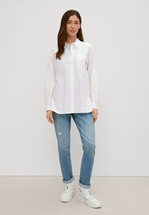 White long-sleeve shirt with a chest pocket, paired with light blue distressed jeans and white sneakers with green accents.
