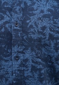 Camicia blu navy con tessuto a motivo fogliare testurizzato di colore blu scuro. Presenta una tasca sul petto e bottoni standard.