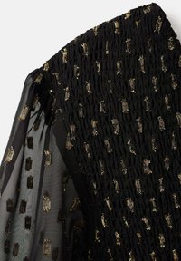 Blusa nera con tessuto arricciato e maniche trasparenti, impreziosita da motivi geometrici e dettagli dorati.