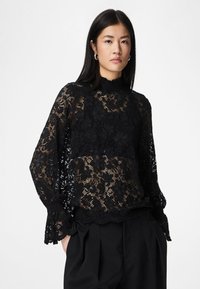 Blusa de renda preta com padrões florais, gola alta e mangas compridas. Apresenta uma bainha ondulada e detalhes intricados por toda a peça.