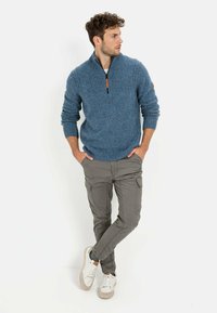 Blauer Strickpullover mit einem Reißverschlusskragen, grauen Cargo-Hosen und weißen Sneakers mit beigen Akzenten. Der Pullover hat gerippte Bündchen und Saum.