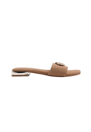 Sandalia tipo slide de ante beige con una tira ancha, emblema metálico decorativo y tacón bajo rectangular plateado.
