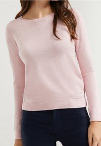 Light pink long-sleeve sweater made of soft knit material. It features a round neckline and a small logo accent at the hem.