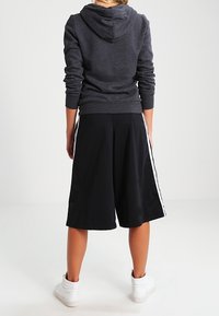 Shorts de sport noirs avec des bandes blanches sur les côtés, associés à un sweat à capuche gris. Le tissu semble doux et décontracté, idéal pour les activités physiques.