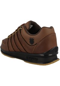 Hnědé kožené tenisky s texturovanými akcenty, černou gumovou podrážkou a zlatými očky. Mají zakřivenou patu a logo na boku.