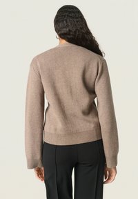 Brązowy sweter o luźnym kroju, z ribbowanymi mankietami i brzegiem oraz teksturowanym materiałem. Nosi się go na czarnych spodniach, prezentując prosty i estetyczny styl.