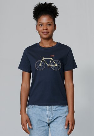 T-shirt en coton bleu marine avec un graphique de bicyclette jaune et une selle marron. Manches courtes et col rond, associé à un jean en denim clair.