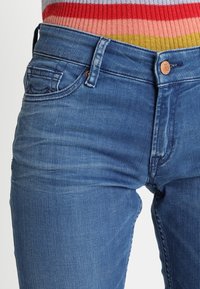 Jeans de mezclilla azul con un diseño ajustado, que presentan un clásico diseño de cinco bolsillos y un cierre de botón de metal en la cintura.