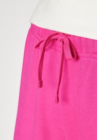 Pink sweatpants with an elastic waistband featuring a drawstring tie. The fabric appears soft and lightweight with a smooth texture.