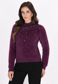 Lilla, fnuggende sweater med høj hals, der har farverige, juvel-lignende udsmykninger foran og ribbede manchetter.