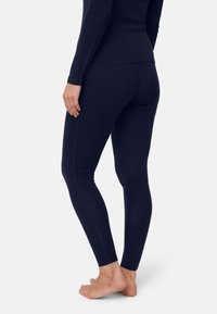 Mörkblå leggings med åtsittande design, slät textur, midjelång midja och kontrasterande sömdetaljer längs sidorna. Barfota modell.