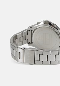 Orologio in acciaio inossidabile argentato con bracciale in metallo, caratterizzato da una cassa rotonda, un fondo piatto e logo inciso sulla chiusura.