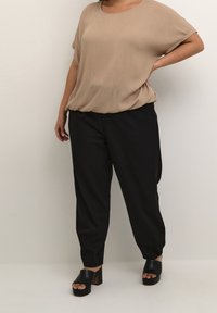 Beige, korte mouwen top in een zachte stof, gecombineerd met zwarte, taps toelopende broeken. Zwarte platform sandalen met een chunky hak maken de outfit compleet.