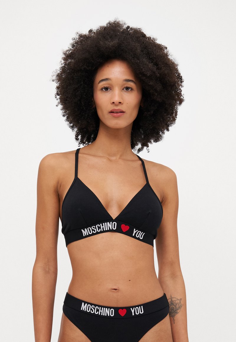 Melns krūšturis un atbilstošas apakšbikses ar logo joslu "MOSCHINO ♥ TEVI." Iespējama trīsstūra kausa dizains un regulējamas siksnas. Mīksts kokvilnas materiāls.