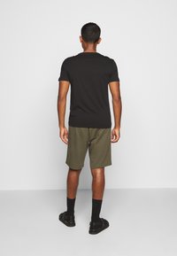 Svart kortärmad skjorta och olivgröna shorts, med svarta sandaler. Slätt tyg, avslappnad passform, synliga stygn på skjortans nederkant.