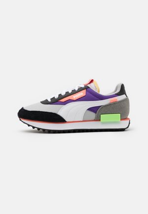 Baskets Puma à profil bas en gris, violet, noir, blanc et orange, avec un bloc vert distinctif au talon et des lacets blancs.