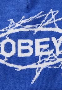 Blauwe gebreide beanie met een wit grafisch ontwerp waarop het woord "OBEY" en abstracte patronen staan, vervaardigd uit zacht wol of acrylmateriaal.