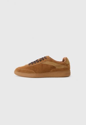 Brązowy zamszowy niski sneaker z ciemnobrązowymi sznurowadłami i gumową podeszwą, widziany od zewnętrznej strony na jasnoszarym tle.