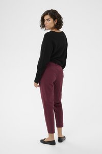 Black sweater, burgundy tapered pants, cropped ankle length. Model stands with back turned, wearing black flats. Smooth fabric texture.