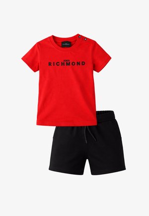 Maglietta rossa a maniche corte con la scritta "JOHN RICHMOND" in nero e pantaloncini neri con coulisse, distesi su uno sfondo bianco.