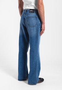 Denim jeans in medium blue, relaxed fit with a straight leg. Features two back pockets and a branded black waistband.