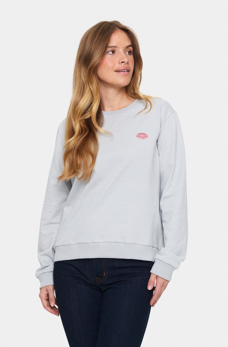 Felpa grigia chiaro con scollo rotondo, polsini e orlo a costine. Presenta una piccola stampa di labbra rosa sul petto. Abbinata a jeans scuri.